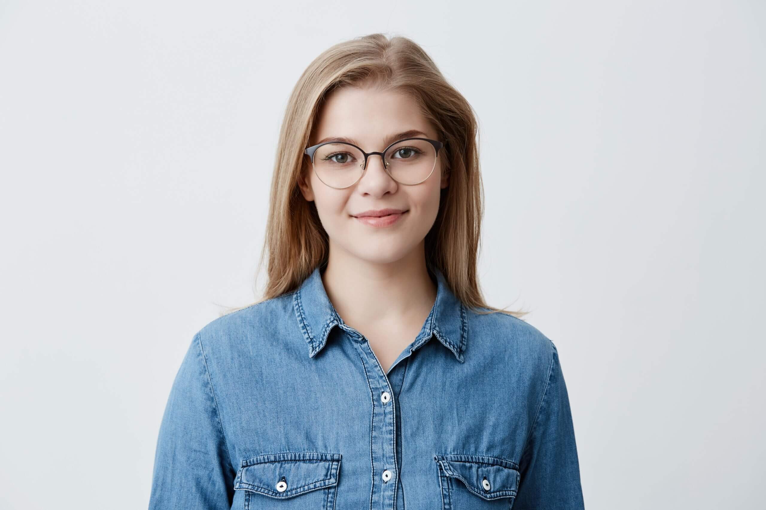 horizontal-portrait-smiling-happy-young-pleasant-looking-female-wears-denim-shirt-stylish-glasses-with-straight-blonde-hair-expresses-positiveness-poses-min-scaled